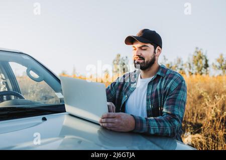 Junger lateinischer Bauer auf seinem Pickup-Truck und mit seinem Laptop. Landwirtschaftliches Konzept. Stockfoto