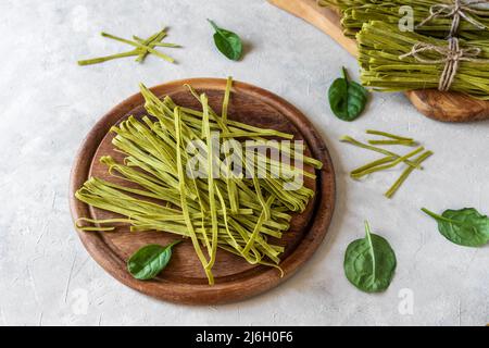 Rohe Pasta Fettuccine mit Spinat auf Holzschneidebrett und Beton Hintergrund Stockfoto