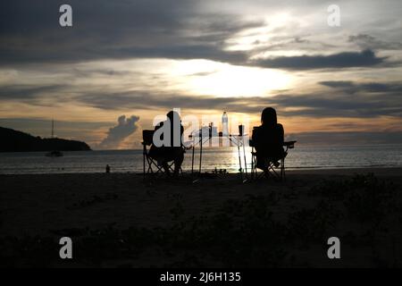 Ein Paar entspannt sich in den Liegen vor dem wunderschönen Sonnenuntergang über dem Meer Stockfoto