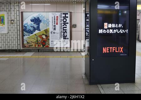 TOKIO, JAPAN - 1. Mai 2022: Bildschirme, die Netflix anzeigen, und ein Plakat, das eine Hokusai-Ausstellung in einer U-Bahnstation in Tokio anwirbt. Die Station ist Iidabas Stockfoto