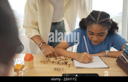 Afroamerikanische Lehrerin steht mit Schülern und unterrichtet Schreibunterricht in modernen Klassenzimmern. Stockfoto