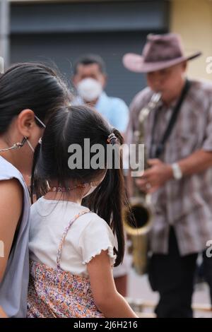 Phuket, Thailand - November 21 2021: Mama und junge Tochter genießen eine Aufführung eines Street Saxophonisten Stockfoto