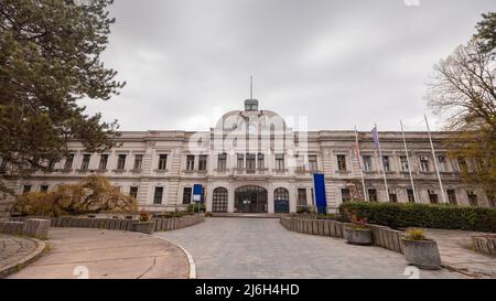 Weißes Gebäude in Kragujevac, großes Kolosseum-Gebäude in der serbischen Stadt, das an einem bewölkten Tag einst das Hauptquartier eines großen Automobilherstellers war. Stockfoto