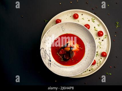 normannische Fischsuppe Bouillabaisse mit Meeresfrüchten auf einem Teller auf schwarzem Hintergrund Stockfoto