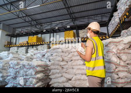 Eine weibliche Lagerarbeiterin trägt eine Maske, die chemische Produkte im Lager von Alaun oder Chemikalien untersucht. Internationales Exportgeschäftskonzept. Stockfoto