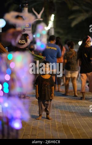 Pattaya, Chonburi Thailand - 11 2021. Dezember: Ein Sohn des Straßenverkäufers, begleitet von seinem Vater, tritt aus der Menge, fasziniert von einem Kameramann Stockfoto