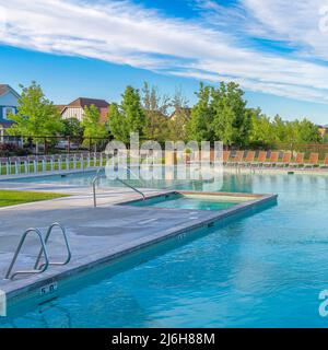 Quadratische, flüsterige weiße Wolken großer öffentlicher Pool, umgeben von Liegestühlen und Drahtzaun in Daybreak, Utah Stockfoto