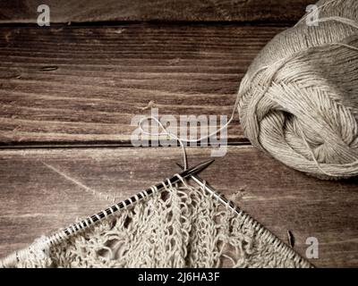 Durchbrochene Tischdecke beim Stricken. Stricknadeln, Schlaufen auf Stricknadeln, Strickstoff, Fadenknäuel, grobe Baumwolle und Leinen Stockfoto