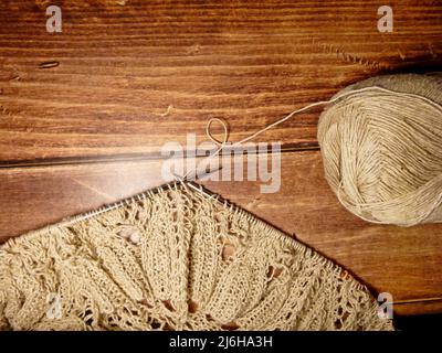 Durchbrochene Tischdecke beim Stricken. Stricknadeln, Schlaufen auf Stricknadeln, Strickstoff, Fadenknäuel, grobe Baumwolle und Leinen Stockfoto