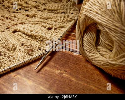 Durchbrochene Tischdecke beim Stricken. Stricknadeln, Schlaufen auf Stricknadeln, Strickstoff, Fadenknäuel, grobe Baumwolle und Leinen Stockfoto