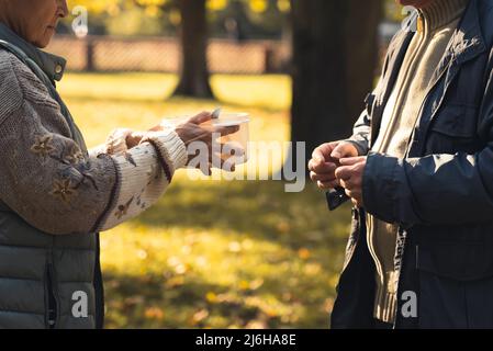 Hände von zwei kaukasischen Obdachlosen, die einen Topf mit hausgemachter Suppe passieren, die von Freiwilligen der Wohltätigkeitsorganisation zubereitet wird. Supportkonzept. Hochwertige Fotos Stockfoto