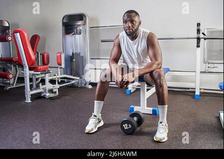 Ein afroamerikanischer Mann sitzt auf einer Bank im Fitnessstudio und ruht sich aus Stockfoto