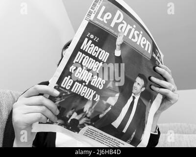 Paris, Frankreich - 25. Apr 2022: Frau liest auf einer gemütlichen Couch die neueste Zeitung Le Parisien berichtet über Frankreichs amtierender Präsident Emmanuel Macron, nachdem er Marine Le Pen für eine zweite fünfjährige Amtszeit geschlagen hatte Stockfoto