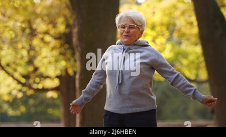 Fitnesskonzept. Im Alter körperlich aktiv zu sein zahlt sich aus. Außenaufnahme der kaukasischen Rentnerin in grauem Hoodie beim Joggen. Hochwertige Fotos Stockfoto