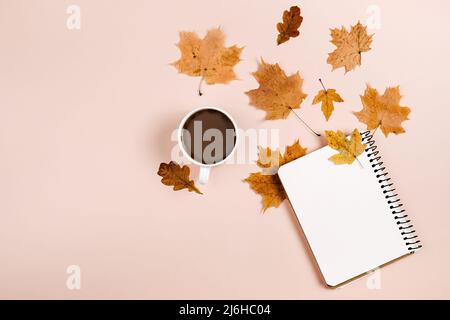 Herbstkomposition. Getrocknete verschiedene Blätter, heiße Kaffeetasse und Notizbuch auf rosa Hintergrundwand im Studio für Werbung. Herbst, Herbst, danke Stockfoto