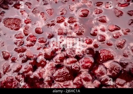 Nahaufnahme von Erdbeergelee, die in einem Topf kocht. Zubereitung von Erdbeergelee, Marmelade oder Erdbeersoße. Machen Sie eine Erdbeermarmelade. Erdbeeren in der Pfanne kochen. Weichfokus, Nahaufnahme Stockfoto