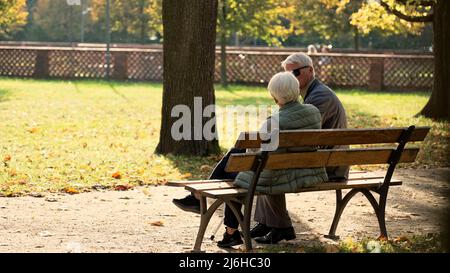 Voller Außeneinsatz mit Herbstkulisse. Rentnerpaar sitzt auf der Bank im Park und genießt das schöne Wetter. Hochwertige Fotos Stockfoto