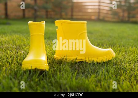 Gelbe Stiefel stehen auf grünem Rasen im Frühlingsgarten - Sommer- und Landleben Konzept Stockfoto