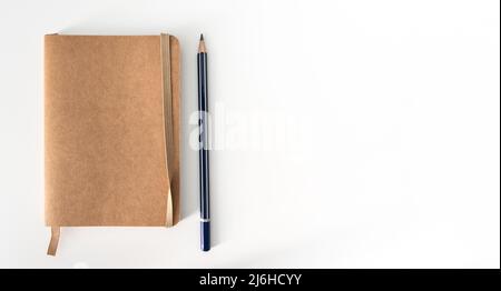 Draufsicht auf ein kleines braunes Notizbuch und einen spitzen Bleistift auf einem weißen Schreibtisch Stockfoto