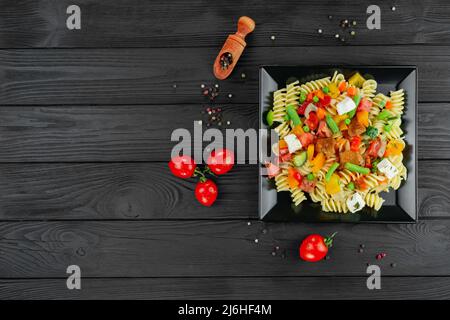 Penne-Pasta mit Gemüse, Erbsen, Paprika, Tomaten, Sauce, Mozzarella-Käse auf schwarzem Holzboden. Italienische Pasta mit Gemüse und sp Stockfoto