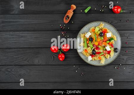 Penne-Pasta mit Gemüse, Erbsen, Paprika, Tomaten, Sauce, Mozzarella-Käse auf schwarzem Holzboden. Italienische Pasta mit Gemüse und sp Stockfoto