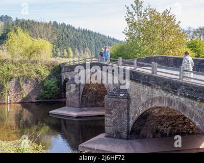 Drei Personen, die über eine mittelalterliche Steinbrücke mit drei Bögen im Vereinigten Königreich laufen Stockfoto