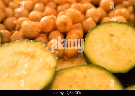 Gewürzte Kichererbsen und Zucchini in Scheiben auf einem Backblech, das bereit ist, in den Ofen gestellt zu werden Stockfoto