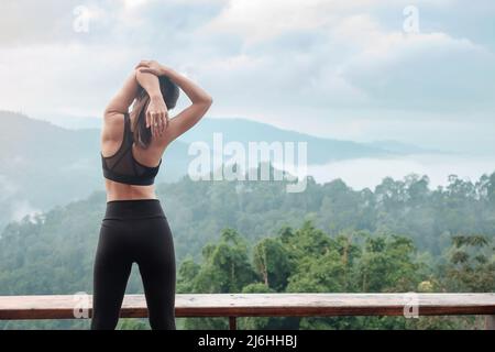 Sportlerin Frau trainiert morgens, junge Fitness-Frau dehnt Muskeln gegen den Bergblick, wärmt sich zum Laufen oder Joggen auf. Workout, gut Stockfoto