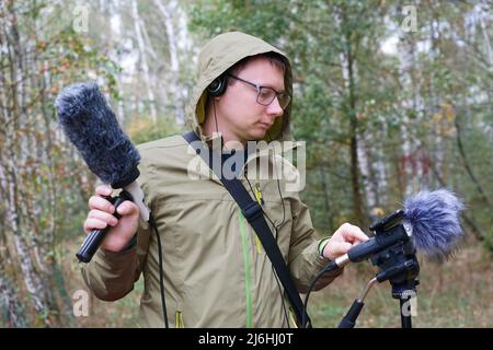 Der Typ mit Shotgun Condenser Mikrofon und Kopfhörern zeichnet die Geräusche der Natur auf. Aufzeichnen Von Umgebungsgeräuschen Stockfoto