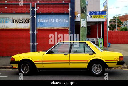 Leuchtend gelbes Oldtimer-Auto des Ford Falcon S, das auf einer heruntergekommenen Straße in Brisbane, Australien, geparkt wurde Stockfoto