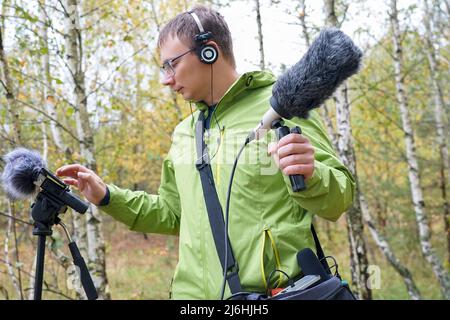 Der Typ mit Shotgun Condenser Mikrofon und Kopfhörern zeichnet die Geräusche der Natur auf. Aufzeichnen Von Umgebungsgeräuschen Stockfoto