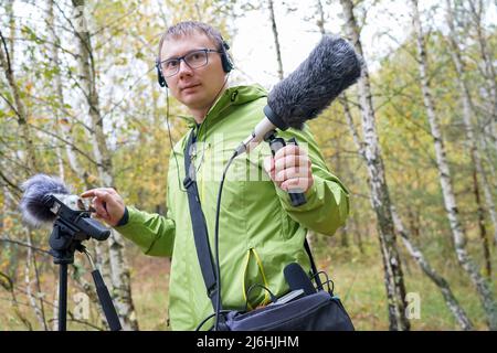 Der Typ mit Shotgun Condenser Mikrofon und Kopfhörern zeichnet die Geräusche der Natur auf. Aufzeichnen Von Umgebungsgeräuschen Stockfoto