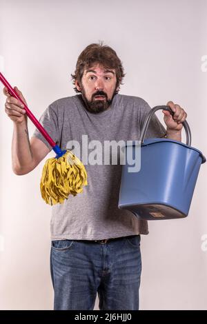 Mann mittleren Alters, kürzlich geschieden, mit Mopp und Eimer. Er weiß nicht, wie er Hausarbeit machen soll. Neuling. Konzept des Menschen in Not. Stockfoto