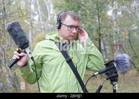 Der Typ mit Shotgun Condenser Mikrofon und Kopfhörern zeichnet die Geräusche der Natur auf. Aufzeichnen Von Umgebungsgeräuschen Stockfoto