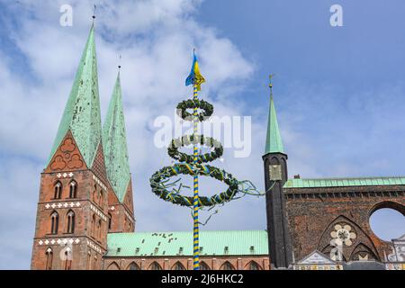 Maibaum in den Farben der Ukraine mit Friedenstauben zwischen den Türmen der Lübecker Marienkirche und dem Rathaus vor blauem Himmel mit Wolken in Ge Stockfoto