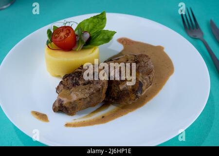 Fleischbällchen mit Kartoffelpüree auf einem weißen Teller. Fleisch in saurer Rahmsoße. Tomaten und Basilikum. Essen im Restaurant. Mittagspause. Medaillons. Stockfoto