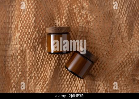 Behälter für Kosmetik und Cremes. Glas braun mit Holzdeckel. Beigefarbener Hintergrund. Monochromes Konzept. Für ein Etikett platzieren. Cremegläser. Schönheit und Pflege. Minimalismus Stockfoto