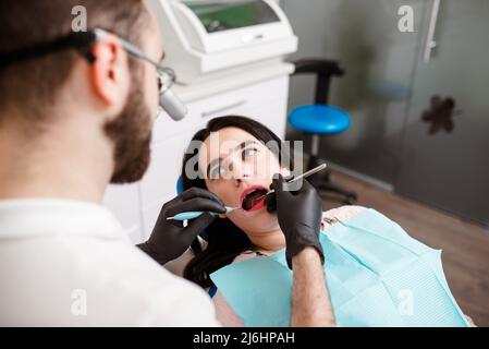 Die schöne junge Frau ist beim Zahnarzt. Sie sitzt auf dem Zahnarztstuhl, und der Zahnarzt legt Zahnspangen auf ihre Zähne, die sich ästhetisch ausrichten Stockfoto