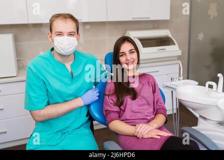 Zufriedene Zahnarztpatientin, die nach der Behandlung in einer Klinikbox mit medizinischen Geräten ihr perfektes Lächeln zeigte Stockfoto