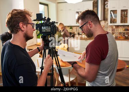 Junger Bediener oder Kameramann, der sich während der Vorbereitung auf das Schießen mit seinem Assistenten oder Kollegen beraten hat Stockfoto