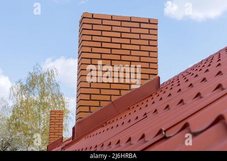 Schornstein auf dem roten Metallkacheldach des Hauses gegen den blauen Himmel Stockfoto