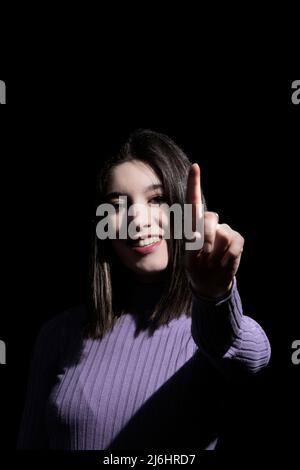 Brünette Frau zeigt den Zeigefinger auf einem schwarzen Hintergrund und weist darauf hin, dass sie die Beste ist Stockfoto