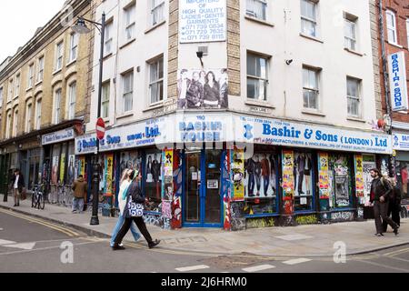 Menschen, die am Bashir House (Bashir & Sons) vorbeilaufen Pakistanisches Geschäft an einer Straßenecke in Brick Lane East London E1, England Großbritannien KATHY DEWITT Stockfoto