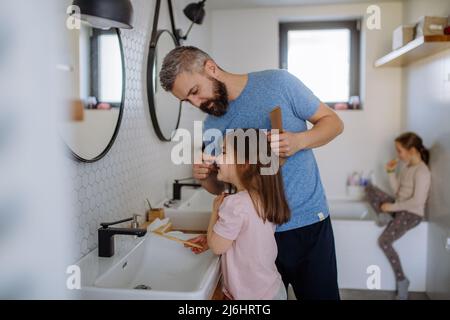 Vater putzt sich die Haare seiner kleinen Tochter im Badezimmer, morgendliches Routinekonzept. Stockfoto