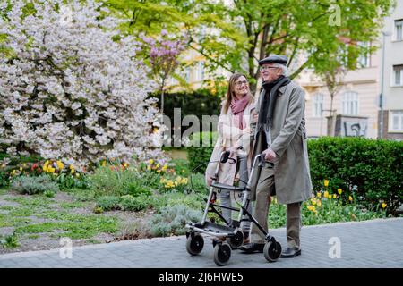 Älterer Mann mit Gehrahmen und Erwachsene Tochter im Freien auf einem Spaziergang im Park. Stockfoto