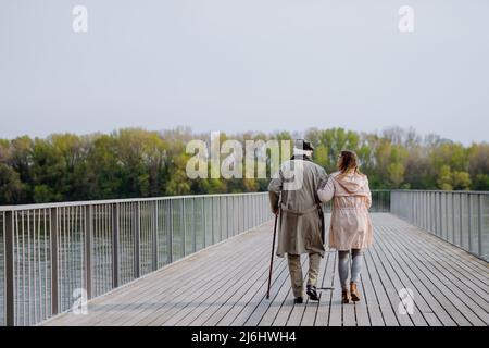 Rückansicht eines älteren Mannes mit Tochter im Freien auf einem Spaziergang am Pier am Fluss. Stockfoto