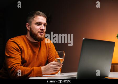 Nahaufnahme eines jungen Mannes, der sich mit einem Laptop fernhält, Glas mit Wein hält und über einen Videoanruf eine Feier anrösten lässt Stockfoto