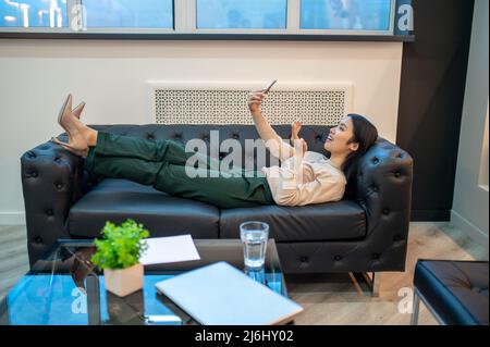 Lächelnde Geschäftsfrau, die in ihrem Büro auf dem Smartphone spricht Stockfoto