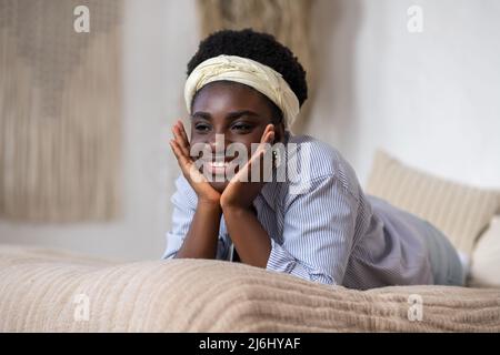 afroamerikanische Frau, die auf dem Bett lag und verträumt aussahnte Stockfoto