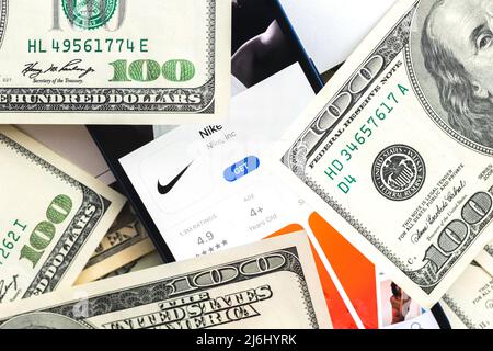 Poltava, Ukraine – 28. April 2022: Logo der Nike Shopping App auf dem Handybildschirm. Geschäftshintergrund mit Laptop und Geld Stockfoto